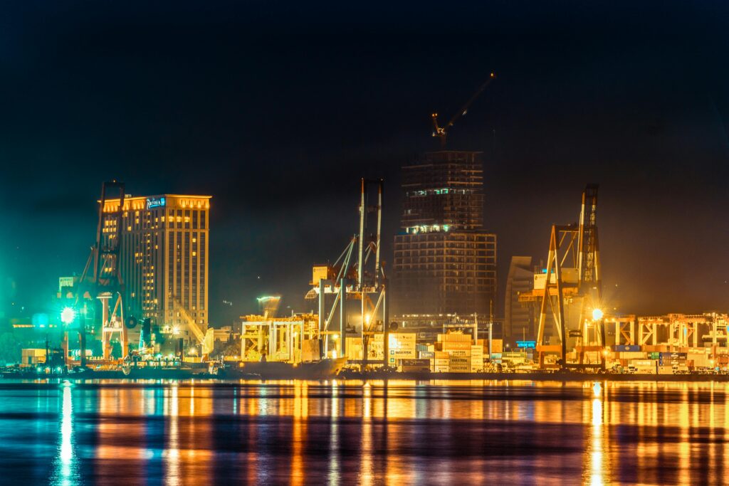 A vibrant city harbor at night with reflecting lights and industrial cranes.